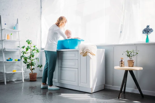Mother washing her little child in plastic baby bathtub at home — Stock Photo