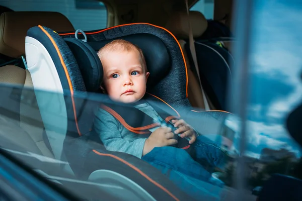 Cute little baby sitting in child safety seat in car and looking through window — Stock Photo