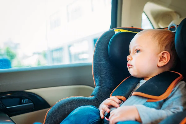 Adorable pequeño bebé sentado en el asiento de seguridad infantil en el coche y mirando a través de la ventana - foto de stock