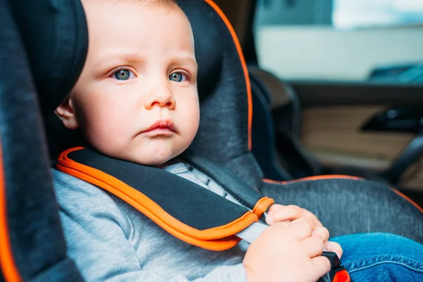 Close-up retrato de pequeno bebê pensativo sentado no assento de segurança infantil no carro e olhando para longe — Fotografia de Stock