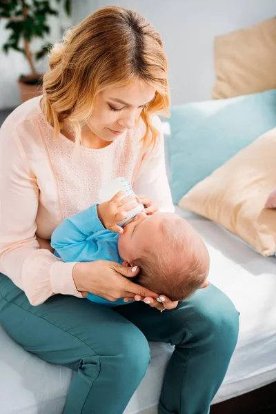 Bela mãe alimentando seu pequeno filho com mamadeira em casa — Fotografia de Stock