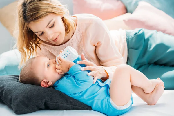 Mother feeding her little child with baby bottle on bed at home — Stock Photo