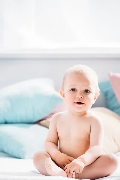 Bebê pequeno bonito sentado na cama e olhando para a câmera — Fotografia de Stock