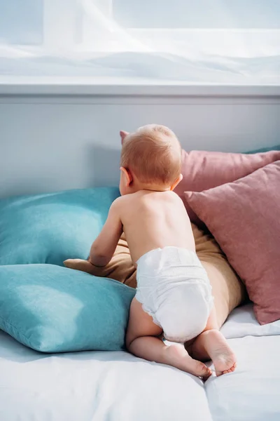 Visão traseira do bebê rastejando na cama com muitos travesseiros — Fotografia de Stock