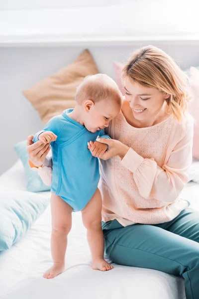 Schöne glückliche Mutter, die ihrem Kind beibringt, wie man zu Hause auf dem Bett geht — Stockfoto