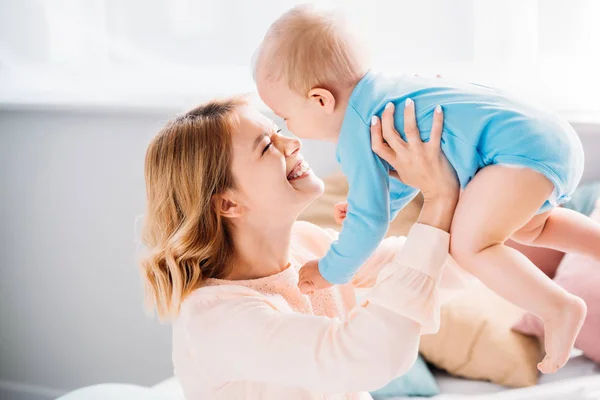 Sonriente madre llevando feliz bebé mientras está sentado en la cama - foto de stock