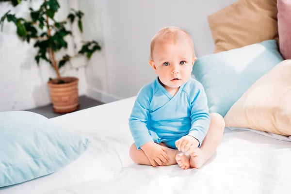 Entzückendes kleines Baby, das zu Hause auf dem Bett sitzt und in die Kamera schaut — Stockfoto