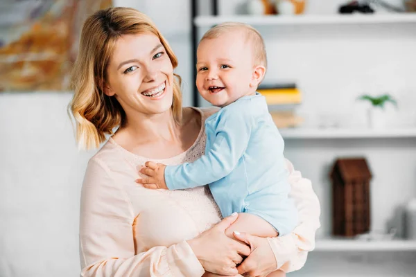 Mother carrying adorable little child and looking at camera at home — Stock Photo