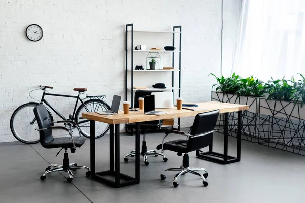 Современный офисный интерьер с ноутбуками и бумажными чашками на столе — стоковое фото