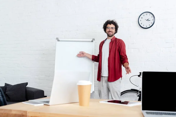 Schöner junger Mann mit Brille, der auf Whiteboard zeigt und in die Kamera lächelt — Stockfoto