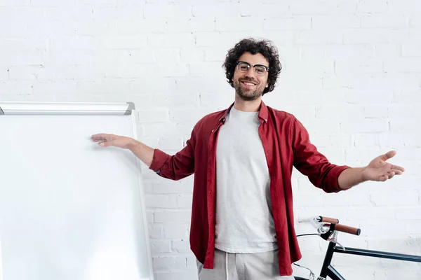 Happy young man in eyeglasses pointing at whiteboard and smiling at camera — Stock Photo