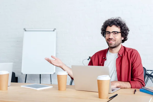 Jeune homme travaillant avec ordinateur portable et souriant à la caméra — Photo de stock