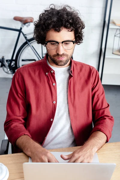 Jeune homme concentré dans les lunettes en utilisant un ordinateur portable sur le lieu de travail — Photo de stock