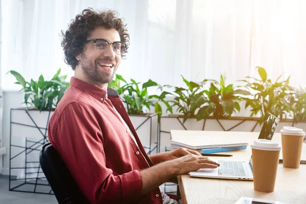 Schöner junger Mann mit Brille, Laptop und lächelnd in die Kamera im Büro — Stockfoto