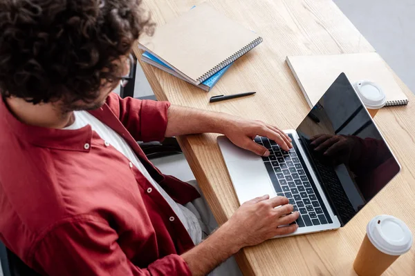 Vista de ángulo alto del hombre joven usando el ordenador portátil con la pantalla en blanco en el lugar de trabajo - foto de stock