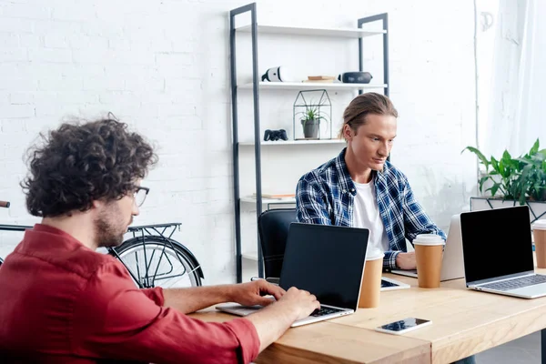 Hombres jóvenes que usan computadoras portátiles mientras trabajan juntos en la oficina - foto de stock