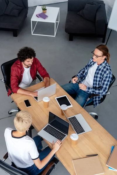 Vue en grand angle des jeunes collègues d'entreprise utilisant des appareils numériques sur le lieu de travail — Photo de stock