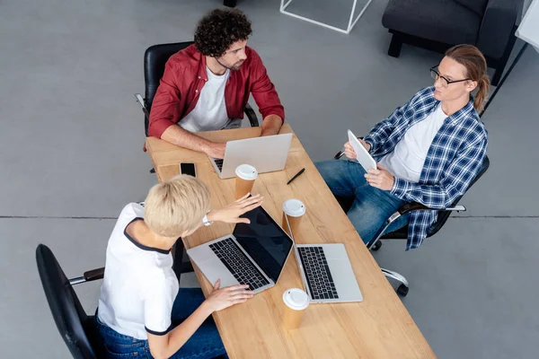 Vista de ángulo alto del equipo joven de puesta en marcha que utiliza dispositivos digitales en el lugar de trabajo - foto de stock