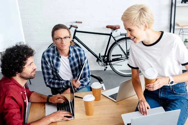 Young start up team using laptops and drinking coffee from paper cups at workplace — Stock Photo