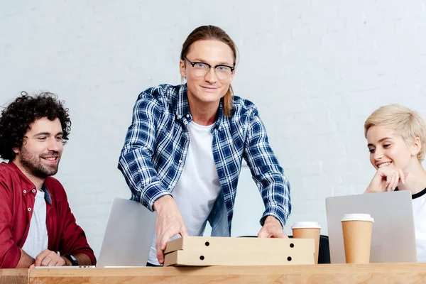 Smiling young colleagues looking at pizza boxes in office — Stock Photo