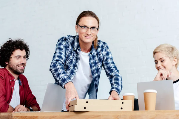 Souriant jeunes collègues regardant des boîtes à pizza dans le bureau — Photo de stock