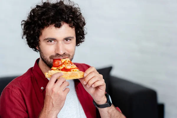 Joven guapo comiendo pizza y mirando a la cámara - foto de stock
