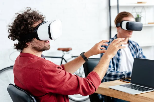 Hombres jóvenes con auriculares de realidad virtual trabajando juntos en la oficina - foto de stock