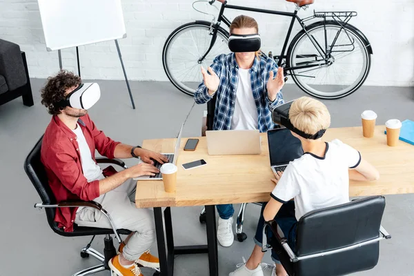Високий кут зору молодих колег у гарнітурах віртуальної реальності за допомогою ноутбуків — стокове фото