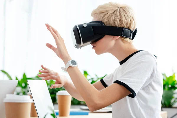 Side view of girl in virtual reality headset using laptop in office — Stock Photo