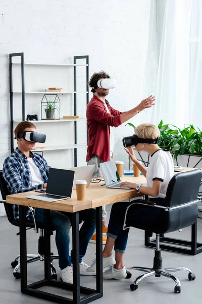Jóvenes que usan auriculares de realidad virtual mientras trabajan juntos - foto de stock