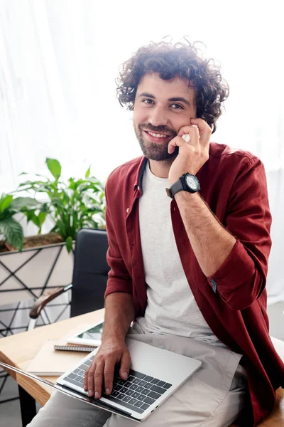 Молодой человек использует цифровые устройства и улыбается перед камерой в офисе — стоковое фото