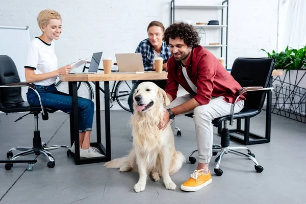 Улыбающиеся молодые бизнесмены, смотрящие на собаку во время работы в офисе — стоковое фото