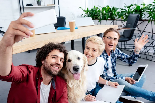 Smiling young people taking selfie with labrador in office — Stock Photo