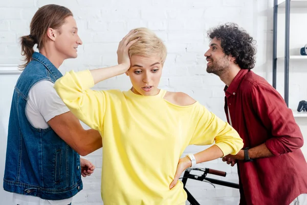 Upset young woman looking down while male colleagues arguing behind — Stock Photo