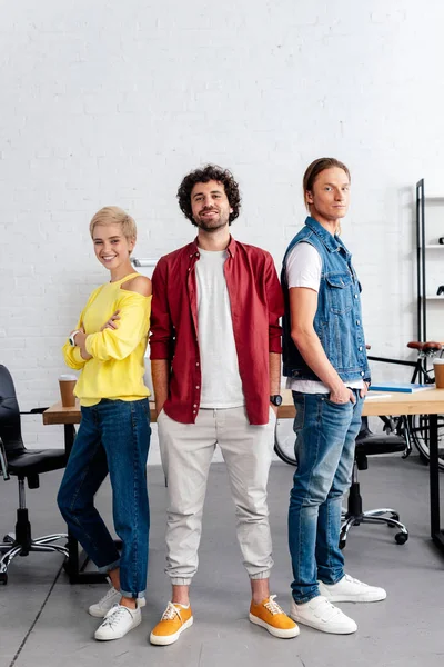 Equipo empresarial joven y seguro de sí mismo de pie juntos y sonriendo a la cámara en la oficina - foto de stock