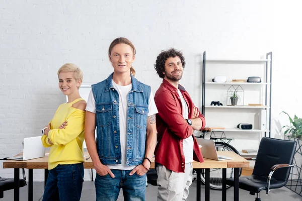 Joven equipo de negocios de pie juntos y sonriendo a la cámara en la oficina - foto de stock