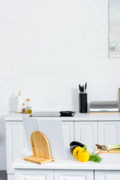 Vegetables and cookbook on kitchen counter in light modern kitchen — Stock Photo