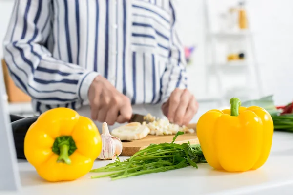 Cropped image of senior woman cooking in kitchen with bell peppers and green onion on foreground — Stock Photo