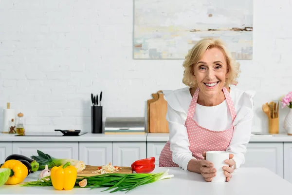 Attraktive Seniorin mit Tasse Kaffee und Blick in die Küche — Stockfoto