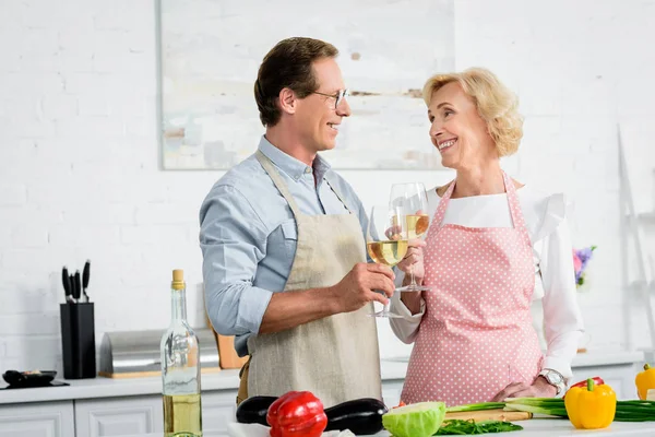 Glückliches Seniorenpaar, das beim Kochen in der Küche mit Weingläsern klingelt und sich anschaut — Stockfoto