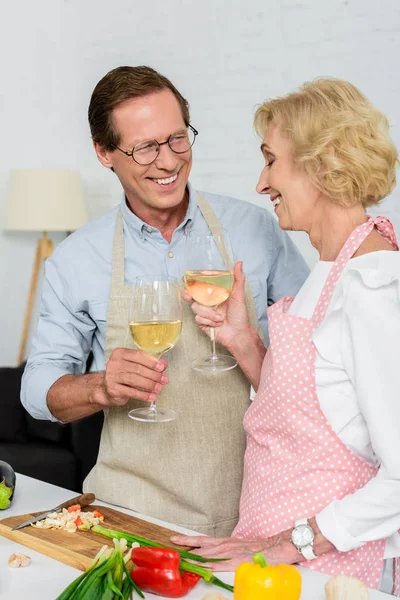 Sonriente pareja mayor tintineo con copas de vino durante la cocina - foto de stock