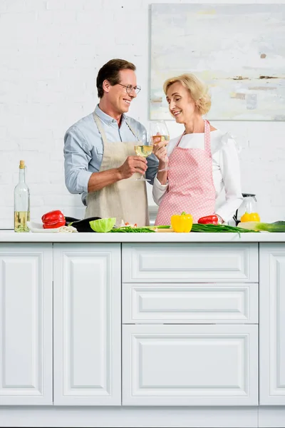 Heureux couple âgé cliquetis avec des verres de vin pendant la cuisson à la cuisine — Photo de stock