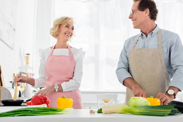 Heureux couple de personnes âgées cuisiner ensemble à la cuisine et en se regardant — Photo de stock