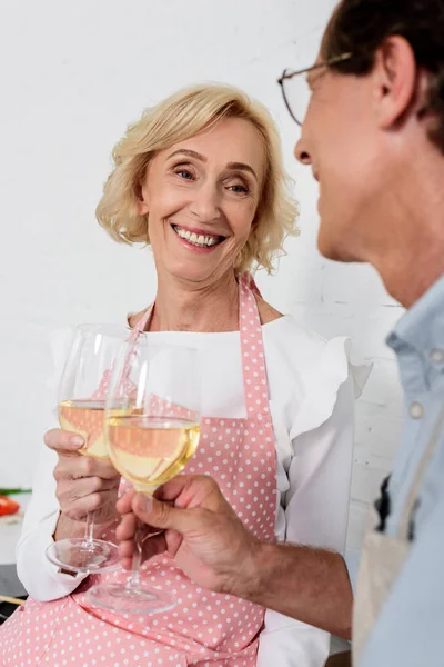 Feliz pareja de ancianos en delantales tintineo vasos de vino mientras cocinan juntos - foto de stock