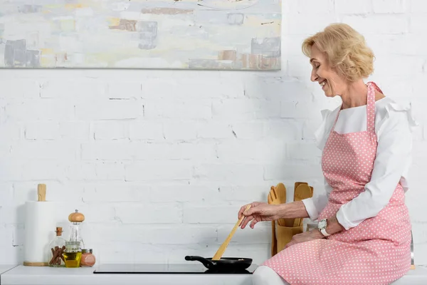 Happy senior woman in apron cooking in kitchen — Stock Photo