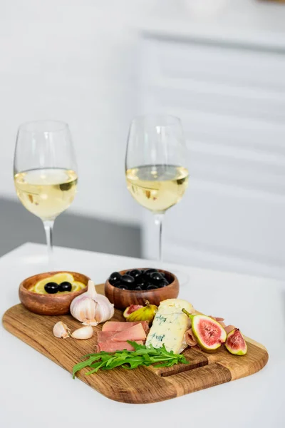 Vista close-up de copos de vinho e deliciosos lanches em tábua de madeira na mesa — Fotografia de Stock