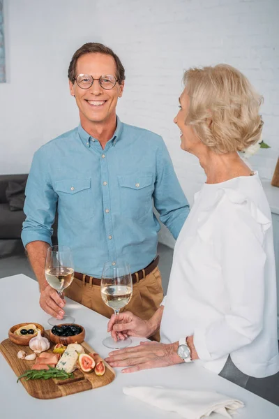 Beautiful happy elderly couple drinking wine and eating delicious snacks at home — Stock Photo