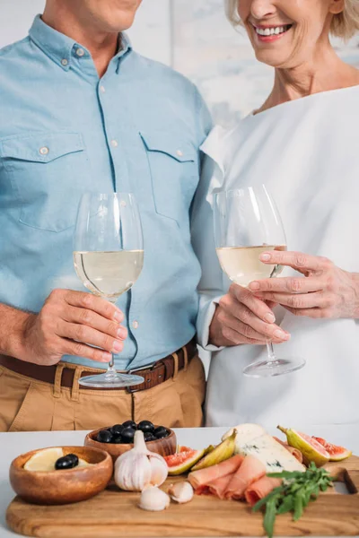 Tiro cortado de casal feliz segurando copos de vinho e comer deliciosos lanches em casa — Fotografia de Stock