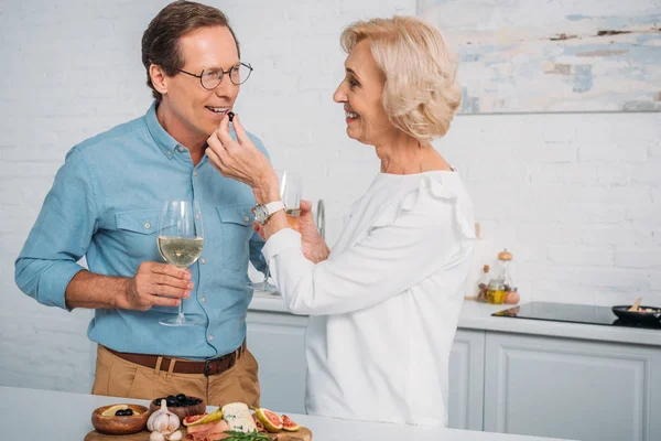 Happy senior couple drinking wine and eating delicious snacks at home — Stock Photo