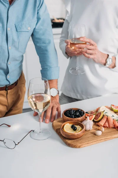 Vista parcial do casal sênior beber vinho e comer deliciosos lanches em casa — Fotografia de Stock